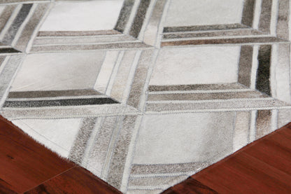 Natural hide indoor hand-stitched rug on wood floor; light gray tones with a subtle irregular pattern and stitched edge.