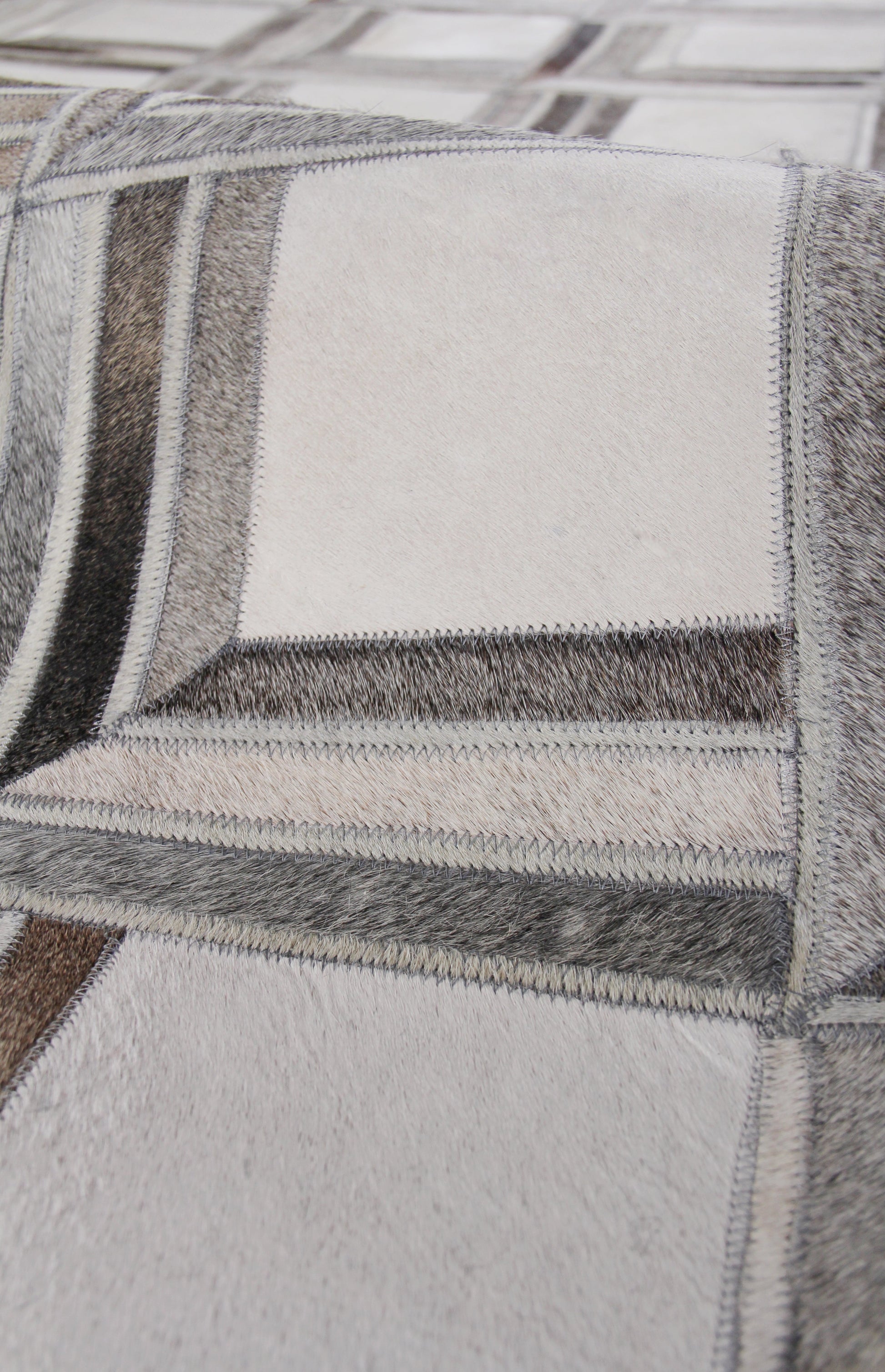 Close-up of patchwork natural hide rug, hand-stitched with zigzag seams in gray, beige, taupe tones.