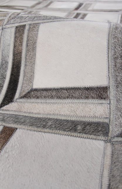 Close-up of patchwork natural hide rug, hand-stitched with zigzag seams in gray, beige, taupe tones.