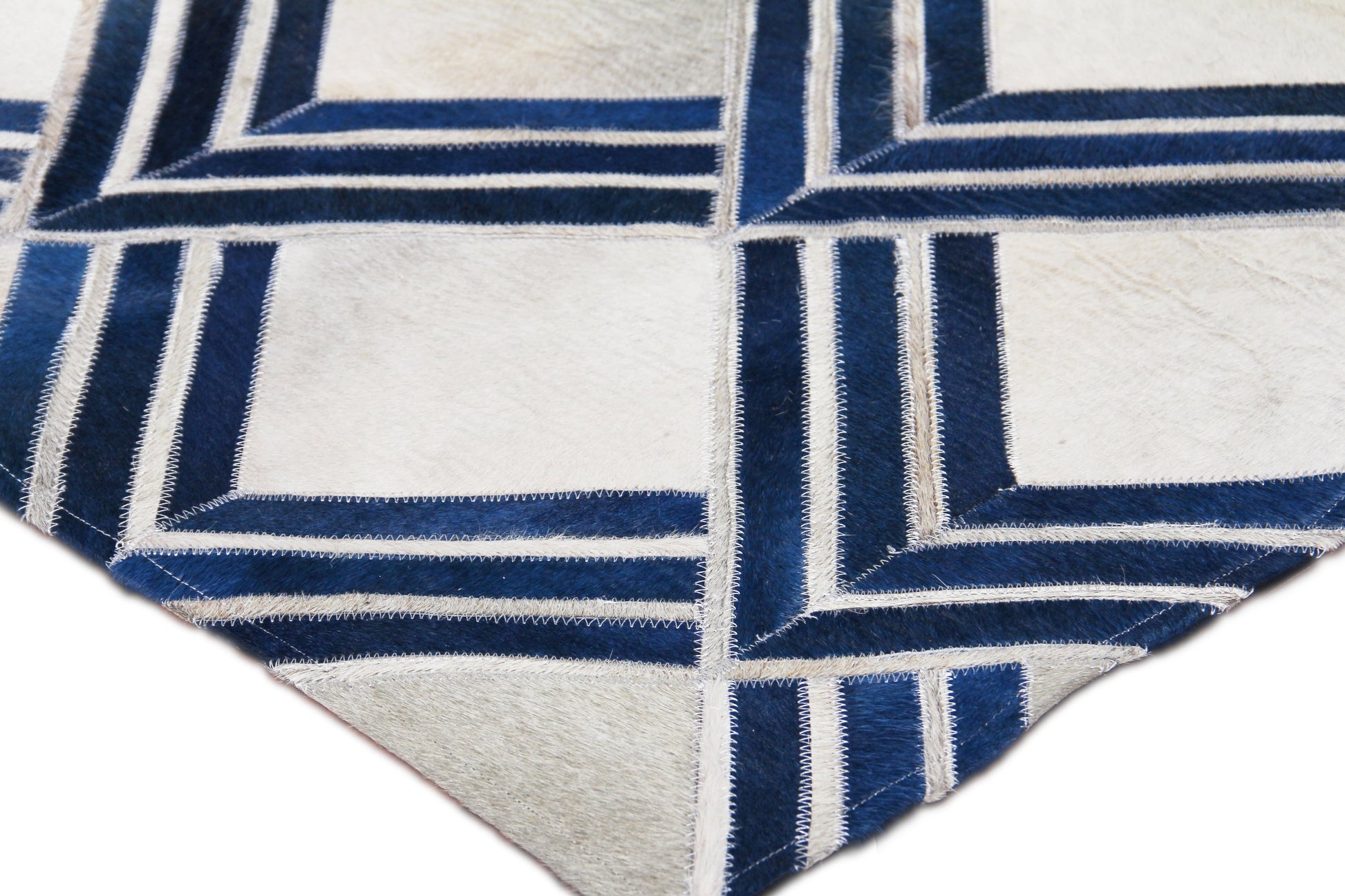 Natural hide indoor hand-stitched rug featuring a geometric blue and ivory interlocking square pattern with navy borders and fringed edges.