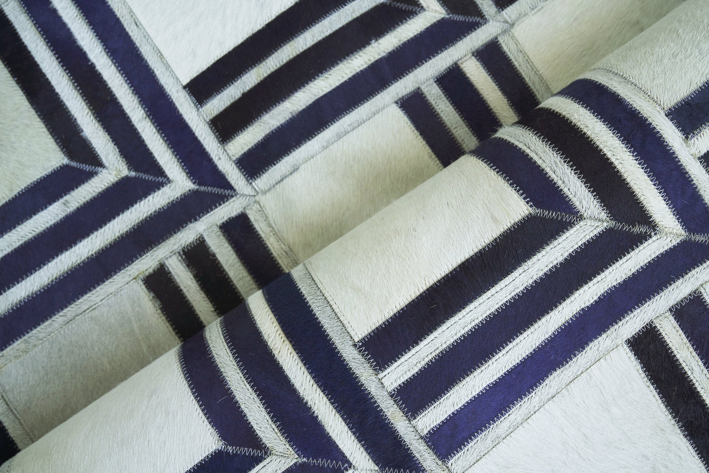 Geometric navy and cream patchwork rug with zigzag stitching; natural hide, indoor hand-stitched rug; 5' x 8'.