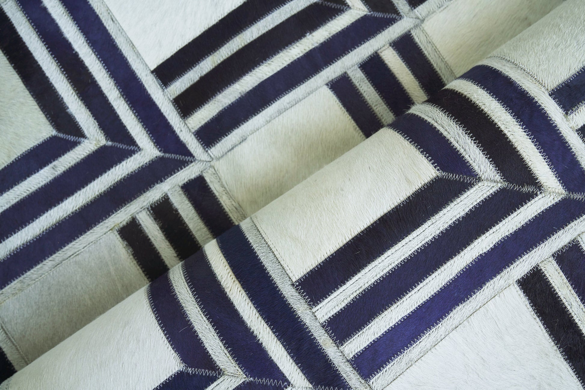 Geometric navy and cream patchwork rug with zigzag stitching; natural hide, indoor hand-stitched rug; 5' x 8'.