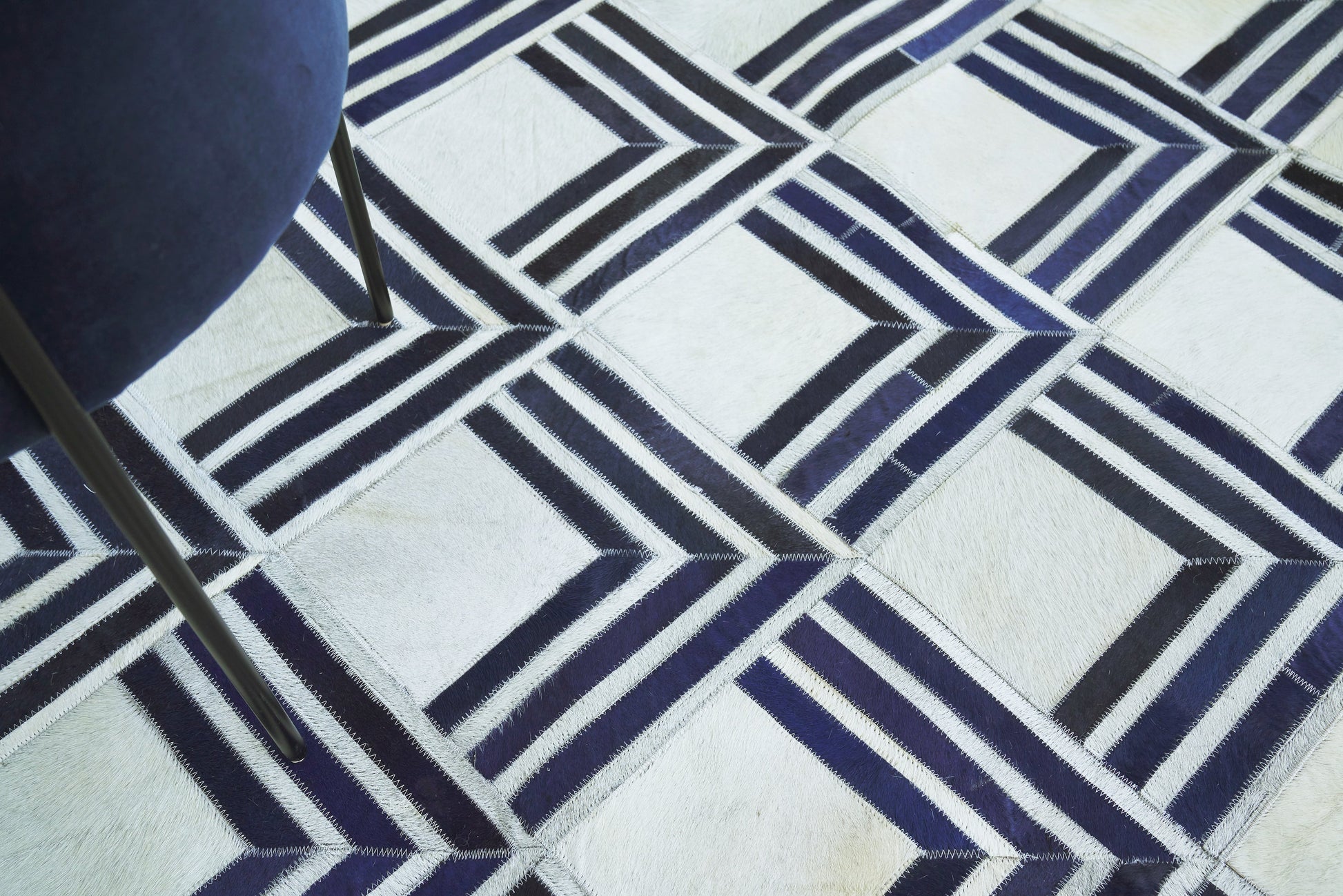 Geometric navy blue and white area rug with interlocking diamond squares; metal chair leg visible on the left.