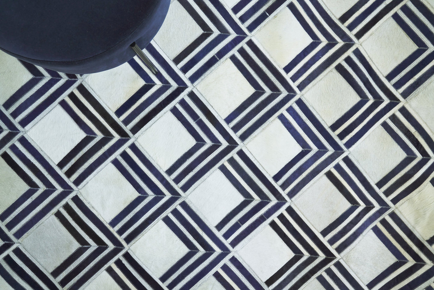 Geometric navy and white rug with interlocking diamond and chevron squares; dark blue ottoman visible in corner.