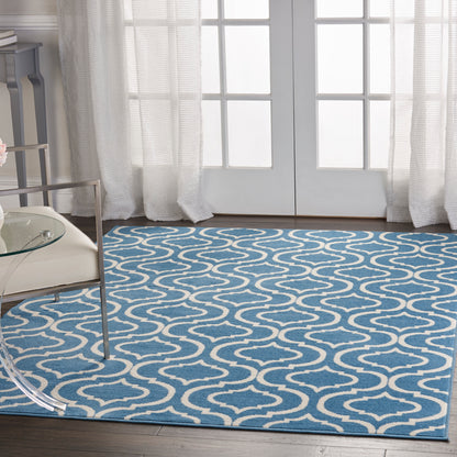 Blue area rug with white wave pattern in front of French doors, with glass coffee table and sheer white curtains.