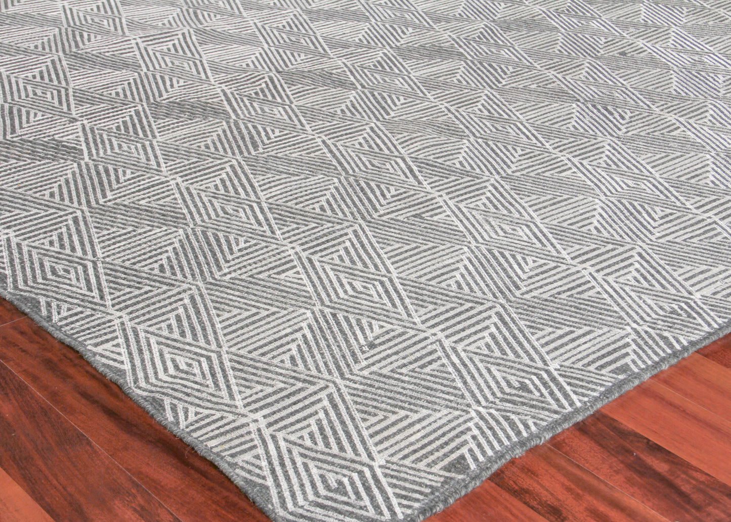 Gray flat-weave rug with white geometric diamond motif on hardwood floor.