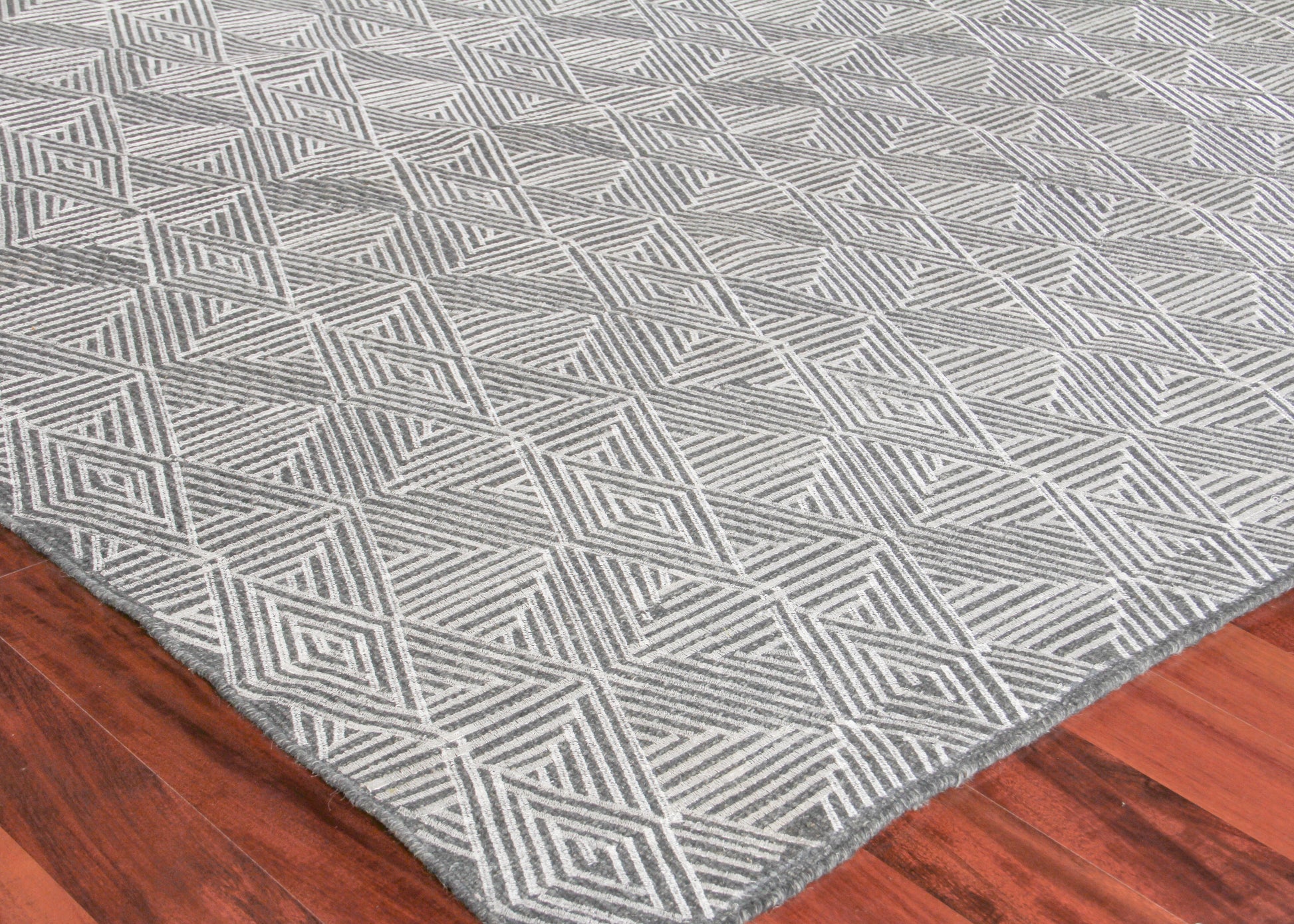 Gray flat-weave rug with white geometric diamond motif on hardwood floor.
