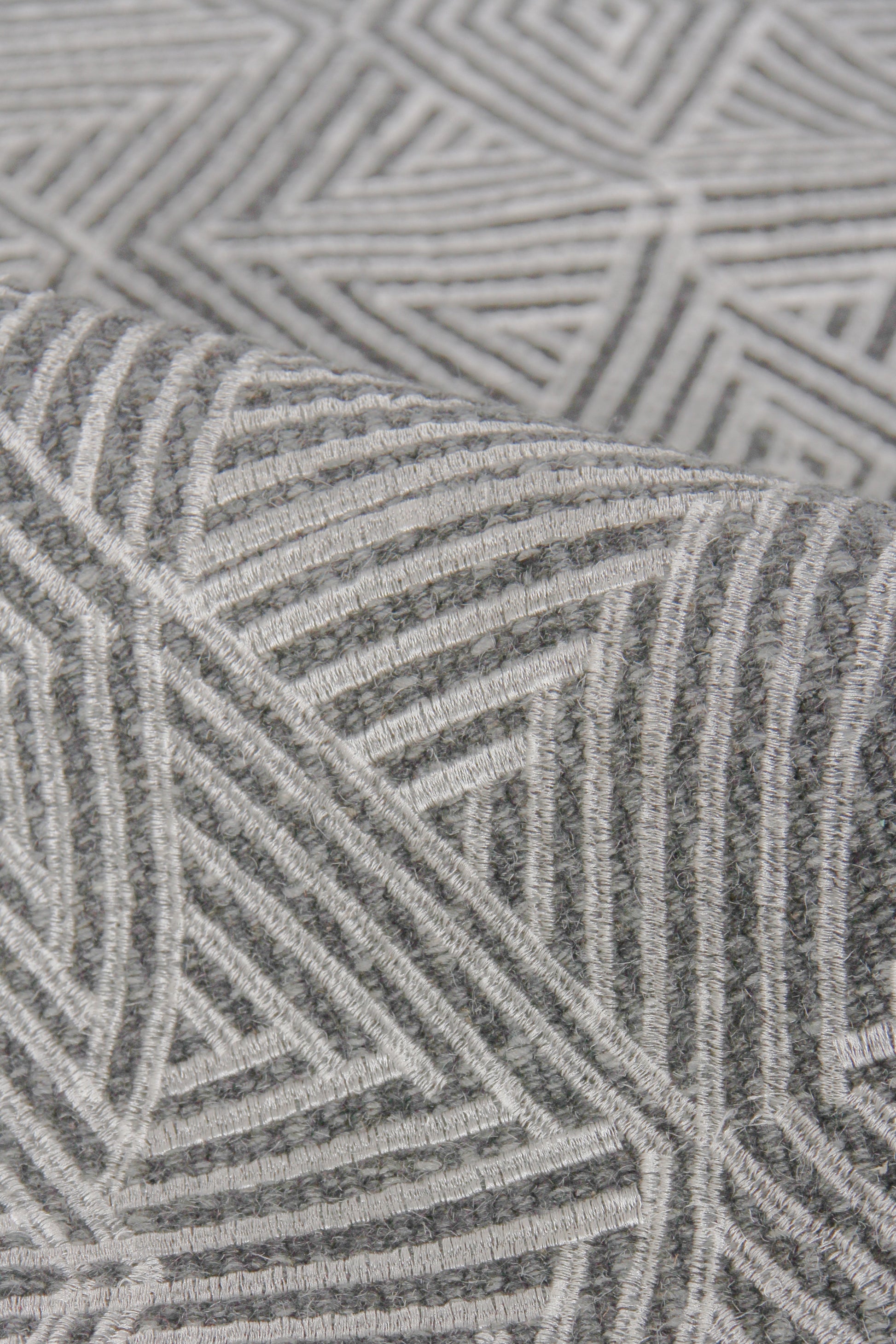 Grey geometric flat-weave rug with white linear chevron and triangle patterns; soft woven texture.