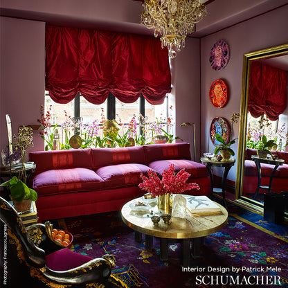 Luxurious red velvet sofa, round marble coffee table, gold accents, chandelier; purple-walled living room with plants.