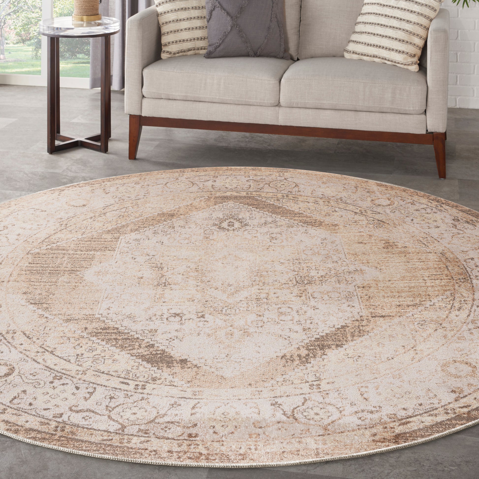 Round beige vintage rug with faded medallion pattern, neutral tones; beside a beige sofa with wooden legs.