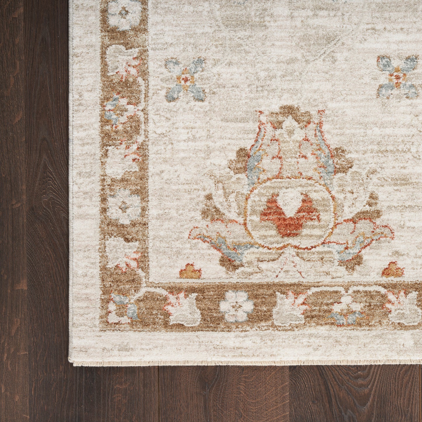 Beige traditional area rug with brown floral border & blue accents on dark wood floor.