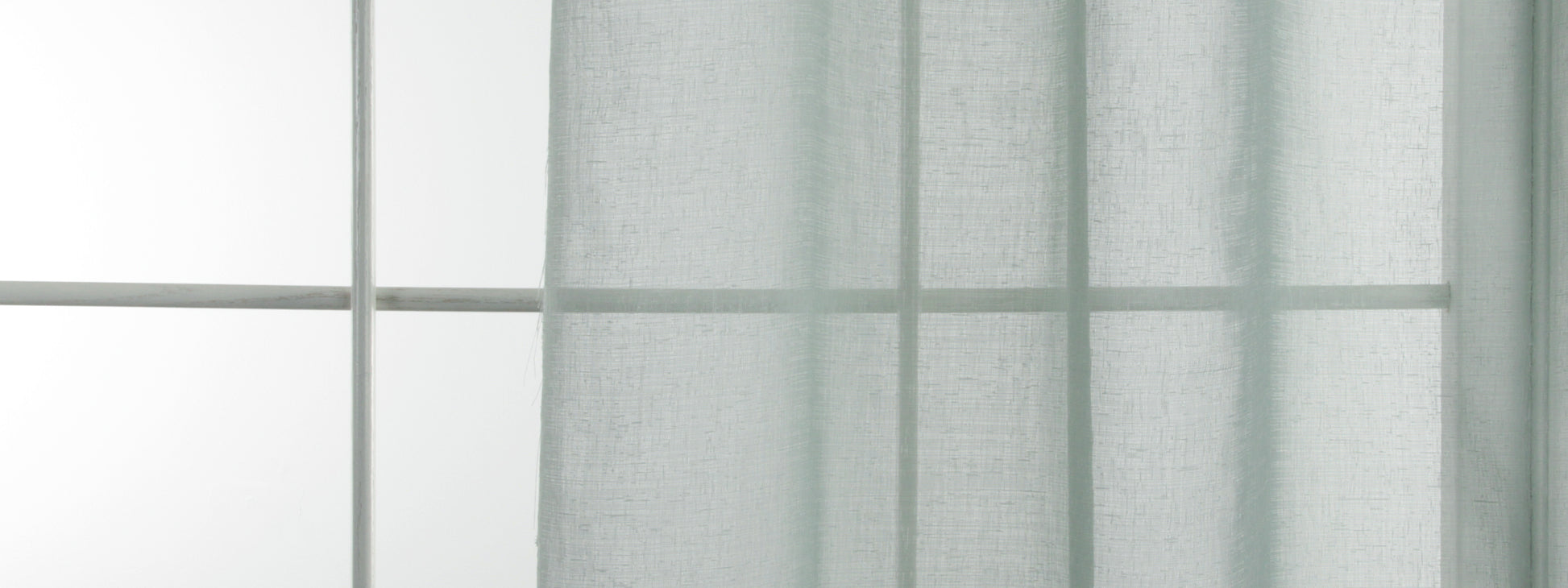 Aquamarine sheer drapery panel in front of a window with grid panes, diffusing soft daylight.