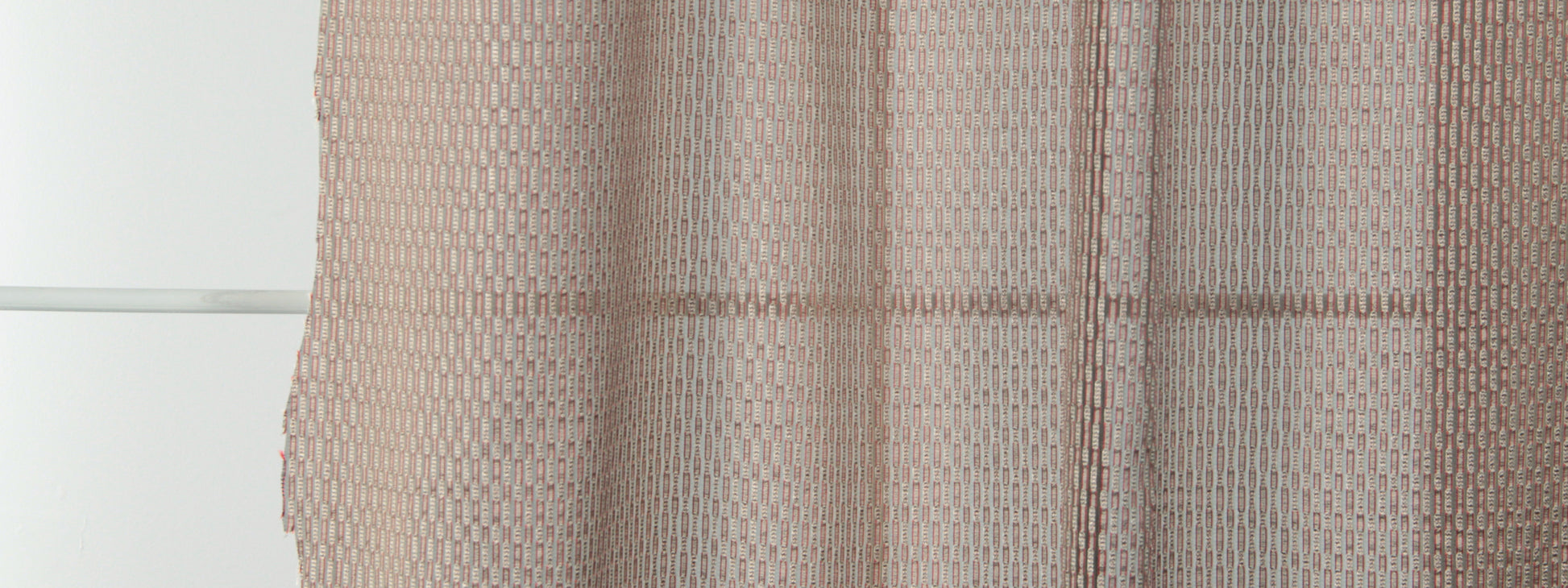 Rust-colored sheer drapery with a subtle geometric weave, light-filtering fabric hanging in front of a window.