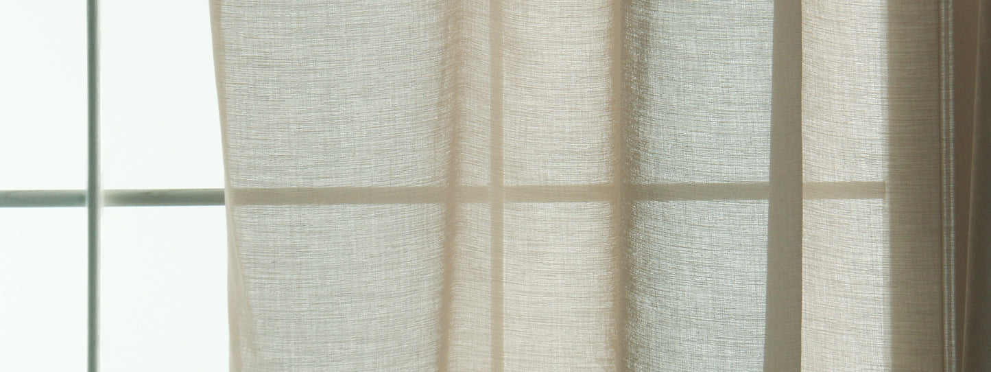 Sand-colored sheer curtains with linen texture hanging by a window, letting soft daylight through.