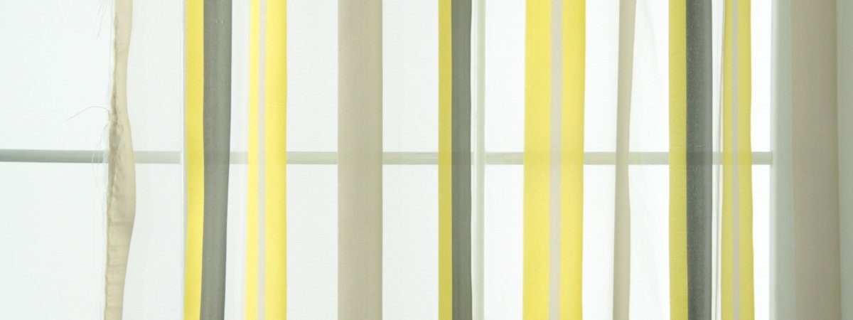 Vertical ribbon curtain strands in yellow, gray and cream, a modern window decor piece.