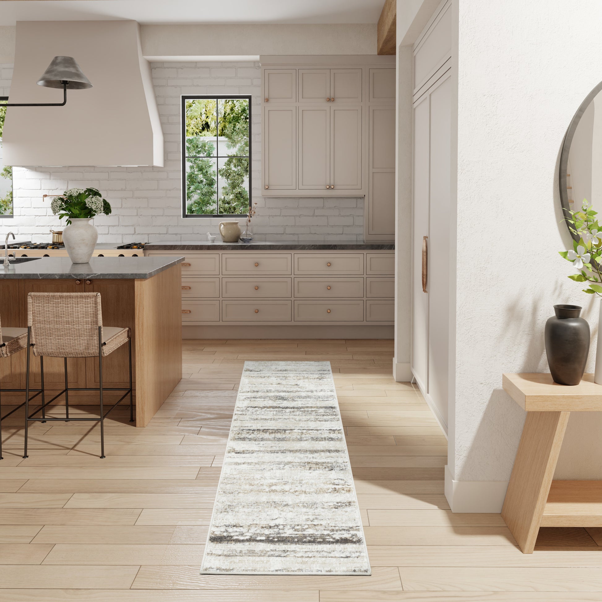 Bright white kitchen with light wood floors, island and stools, cabinets, subway tile, and a distressed gray rug runner.