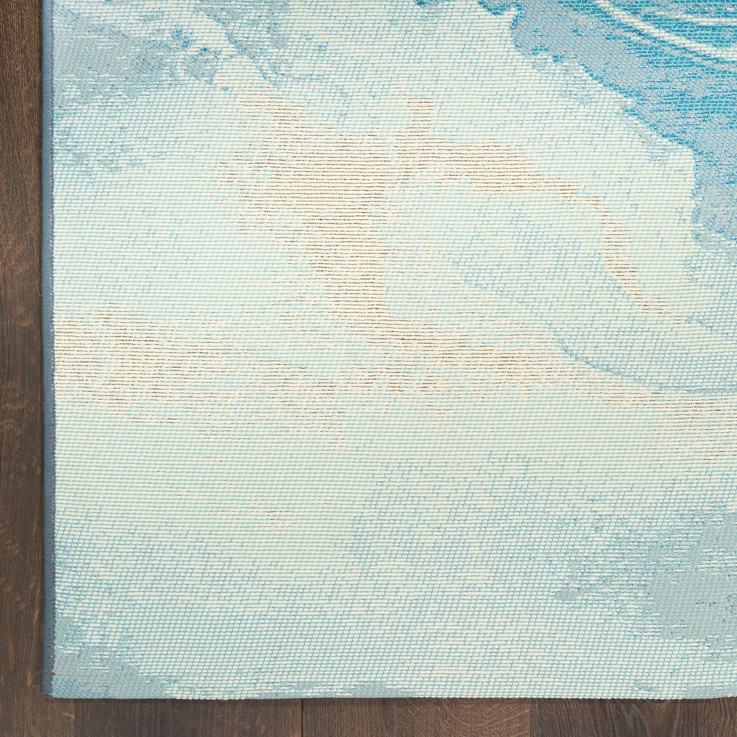 Blue pastel woven area rug with abstract beige shapes, slim blue border, on a wooden floor.