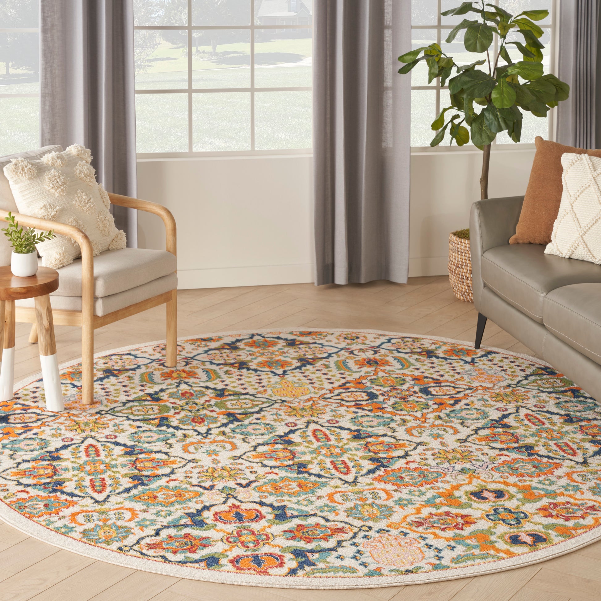 Round multicolor floral area rug on light hardwood floor with beige armchair, gray sofa and leafy plant.