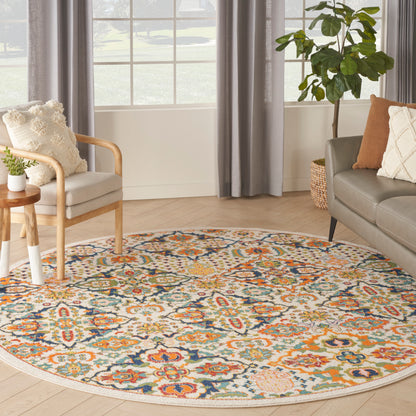 Round multicolor floral area rug on light hardwood floor with beige armchair, gray sofa and leafy plant.