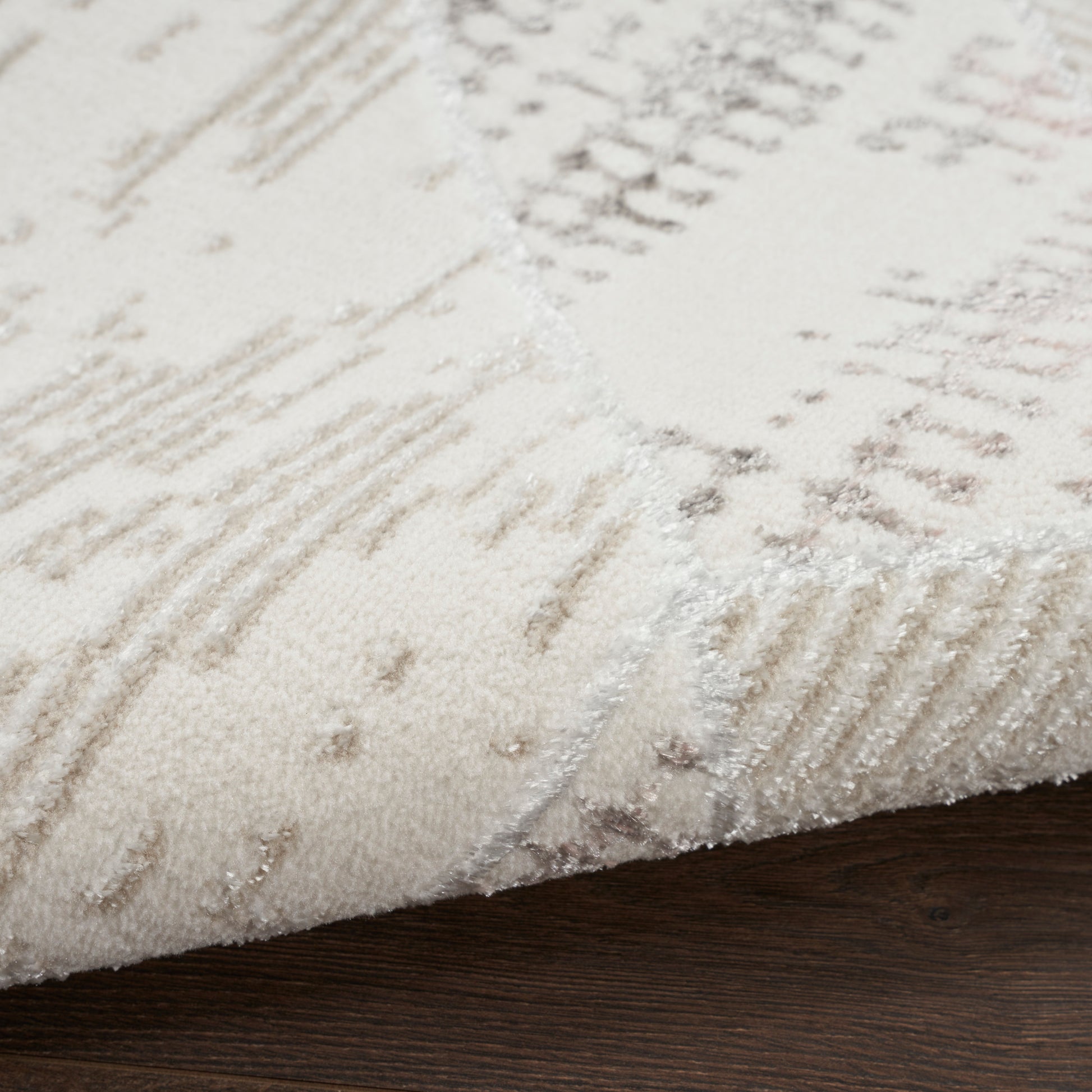 Close-up of a cream rug with taupe geometric patterns & soft texture, edge folded over dark wood floor