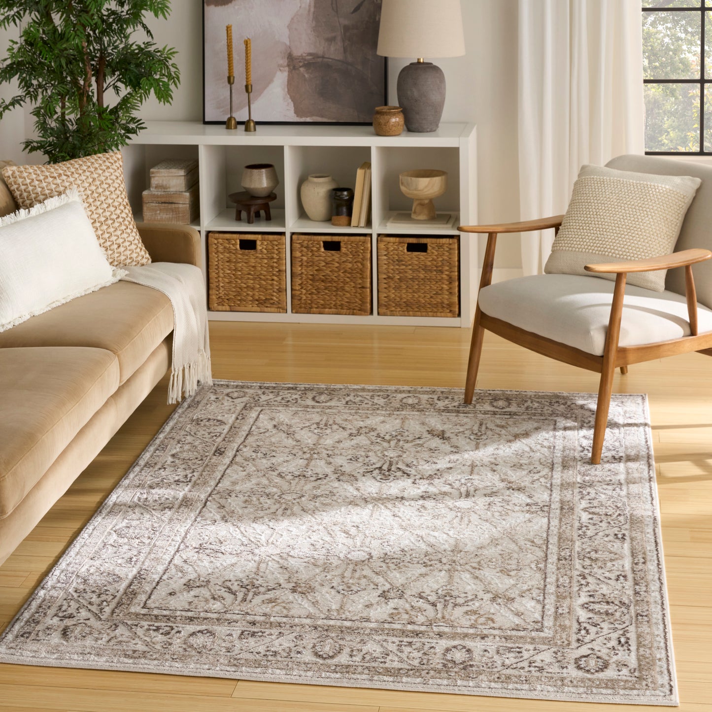 Neutral living room with light grey ornate area rug, beige sofa, wooden chair, white cubby shelves, and woven baskets.