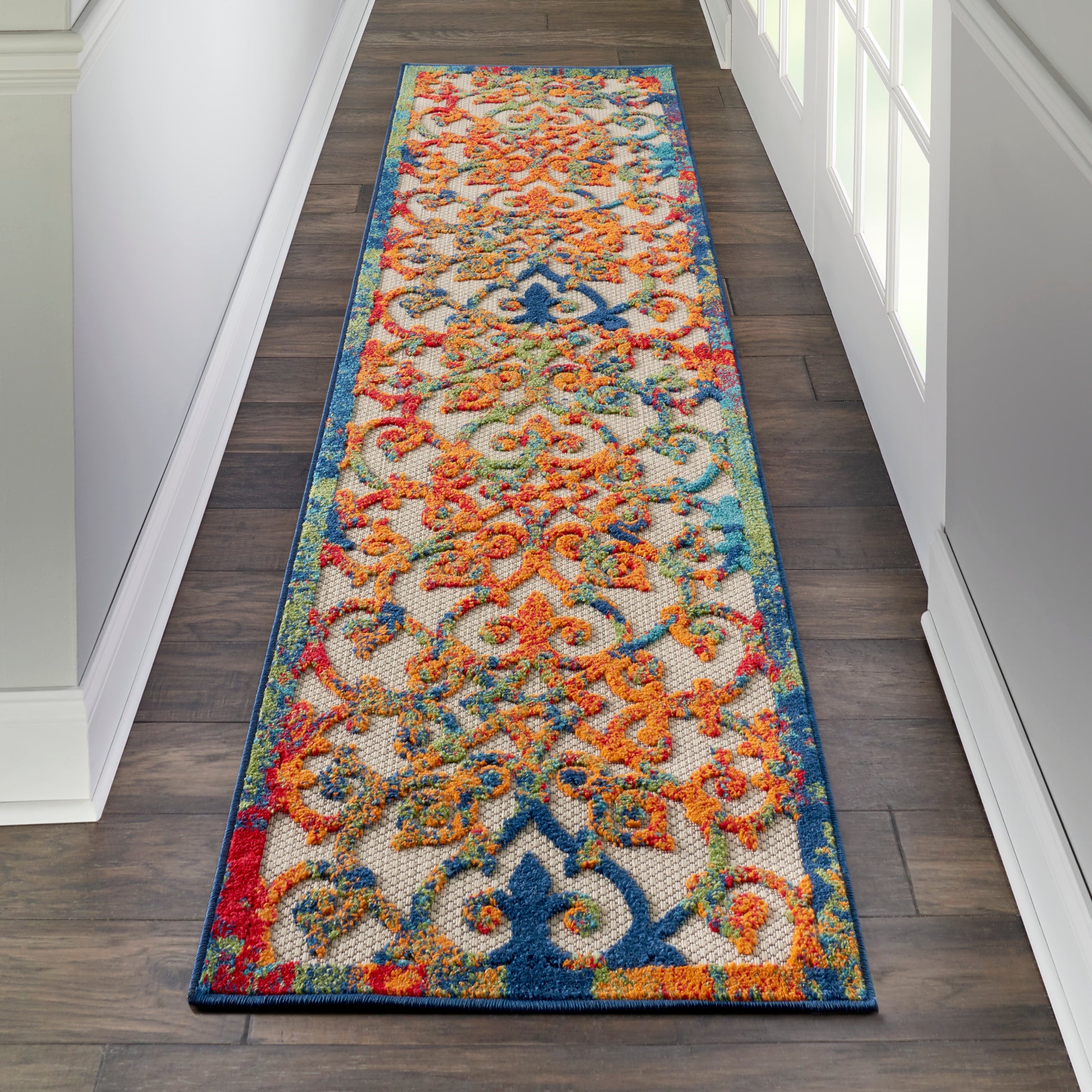 Long hallway runner rug with ornate multicolor pattern, blue border and orange/teal motifs on ivory, low-pile flatweave.