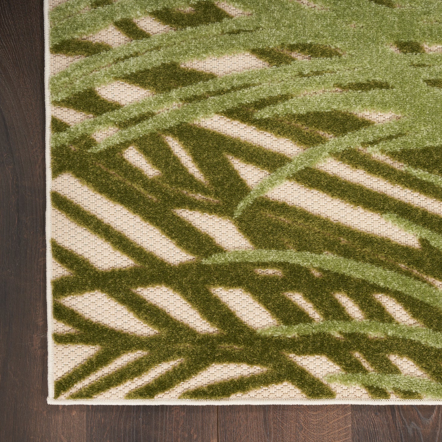 Green palm-leaf patterned outdoor rug on beige woven background with white border, shown on dark wood floor.