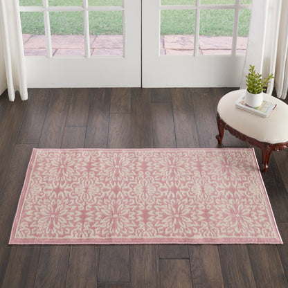 Rectangular pink rug with cream damask pattern on dark wood floor near French doors, beside a small side table with plant.