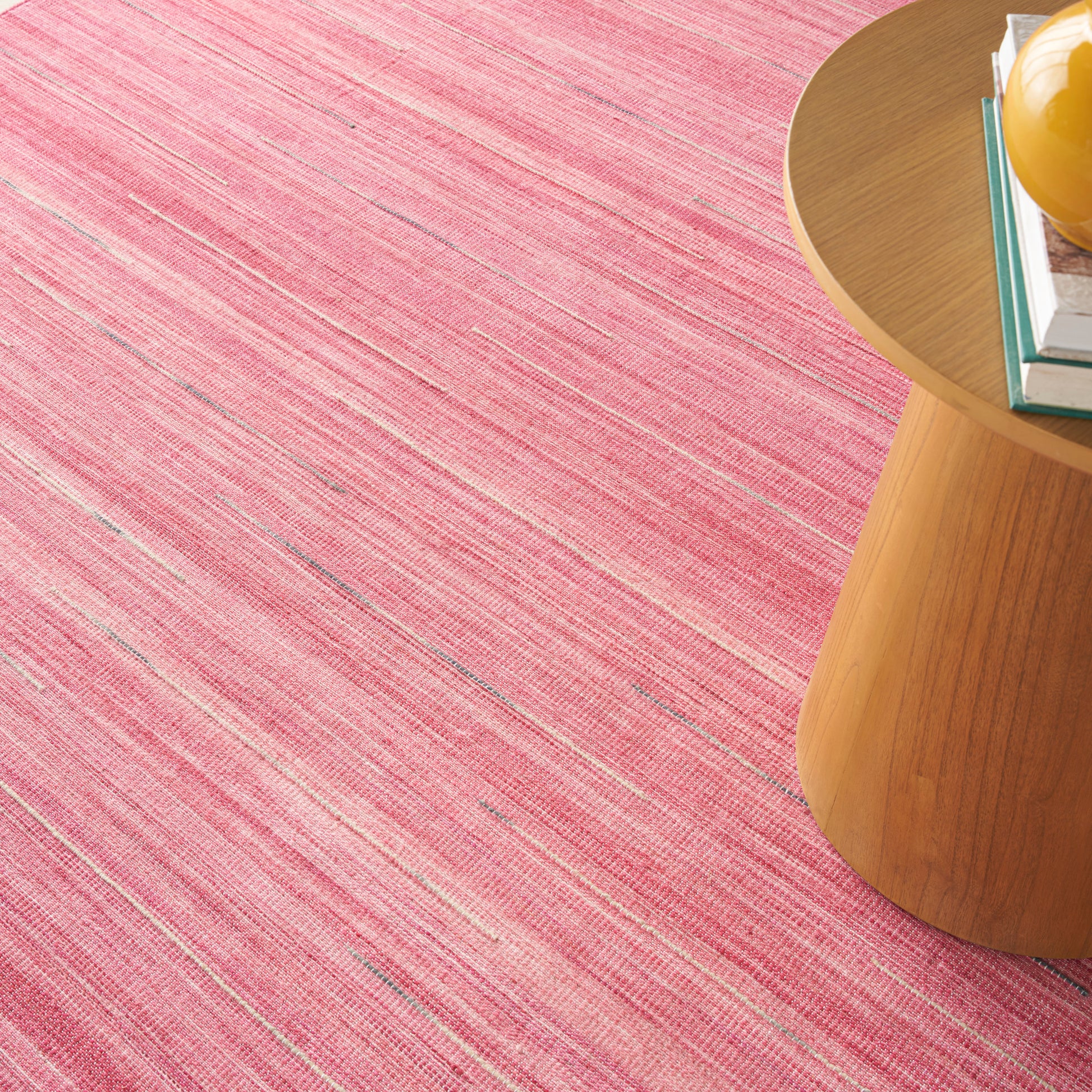 Pink striped rug on the floor with a round wooden side table holding a yellow hard hat and stacked books.