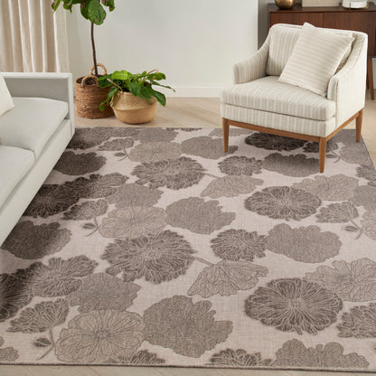 Living room with a large beige floral area rug, cream striped armchair on wooden legs, light sofa, and potted plants.