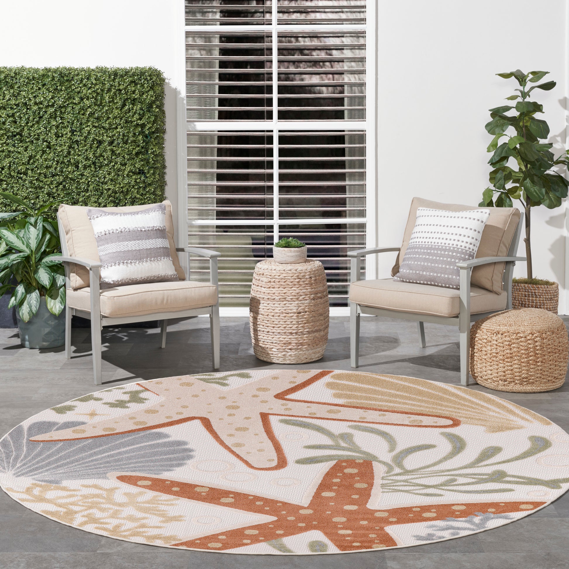 Outdoor patio with beige cushioned metal chairs, coastal rug in orange starfish motif, wicker table and ottoman, plants.