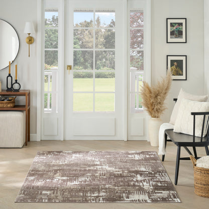 Brown and ivory abstract area rug on a light wood floor in a bright living room with minimalist decor.