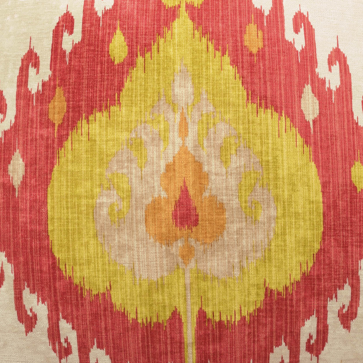 Pillow with ikat-inspired fabric: red outer border, cream accents, and a yellow center teardrop motif.