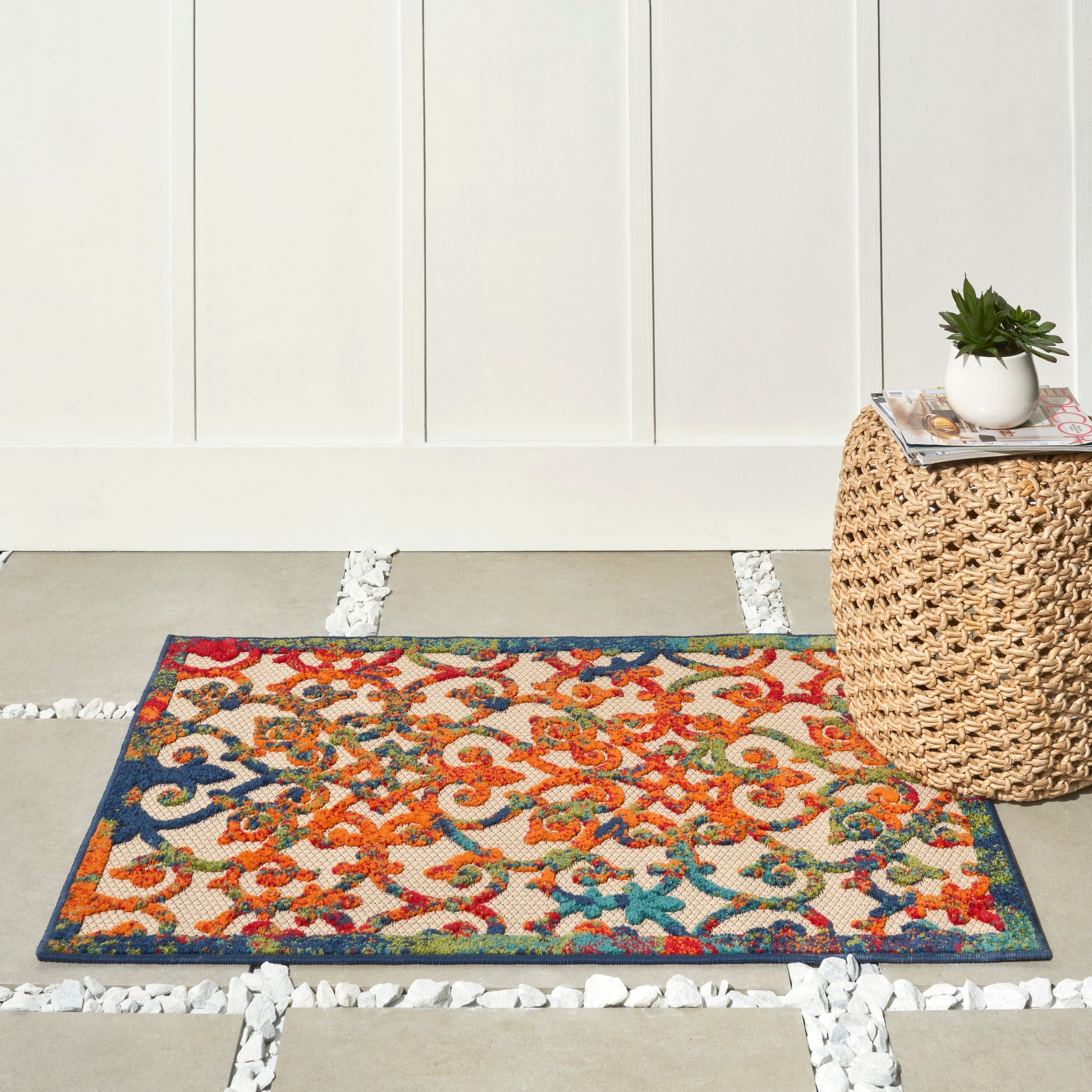 Colorful oriental-style rug with red/orange floral motifs and blue border on a light floor beside a woven rattan table.