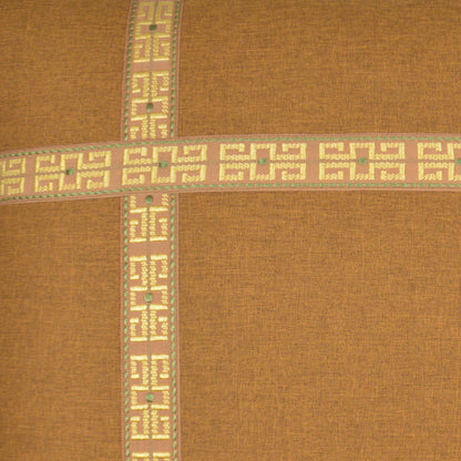 Pillow cover in burnt-orange fabric with beige Greek-key cross bands & mint green/pink accents; visible woven texture.