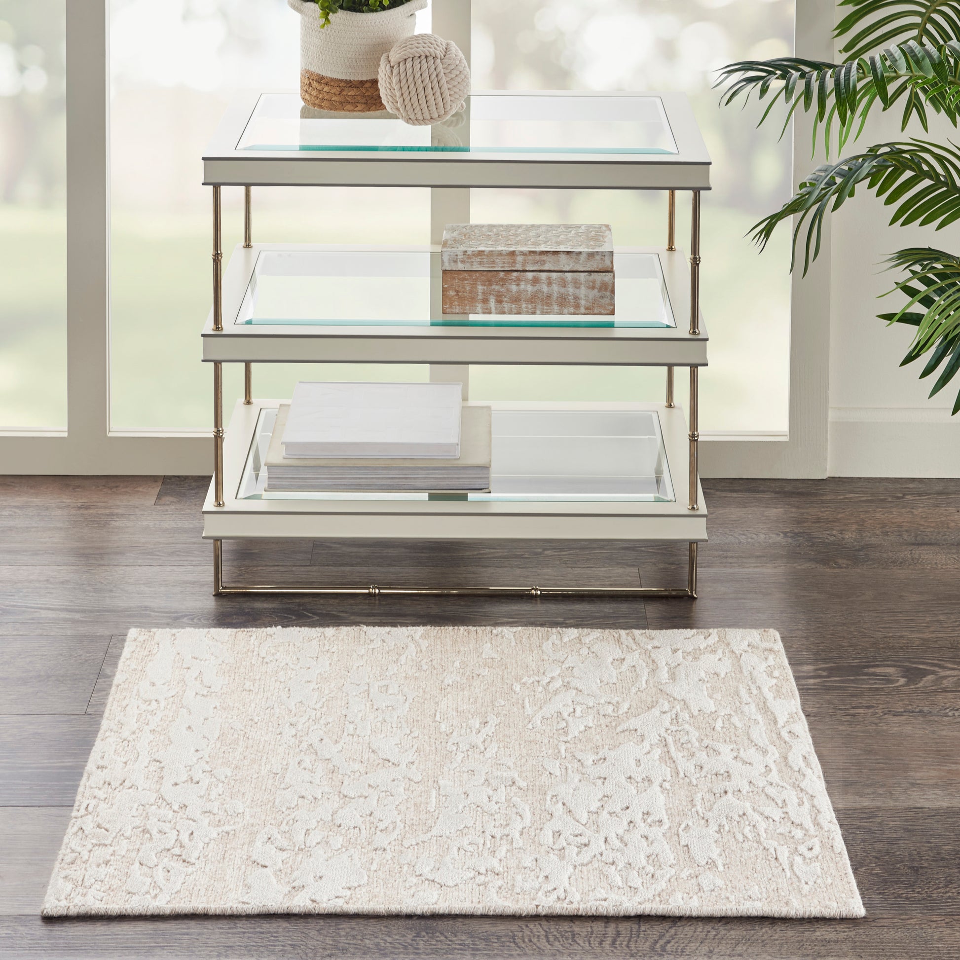 Beige rug on dark wood floor with yarn ball, wooden box, and stacked books nearby; size 2' x 3'.