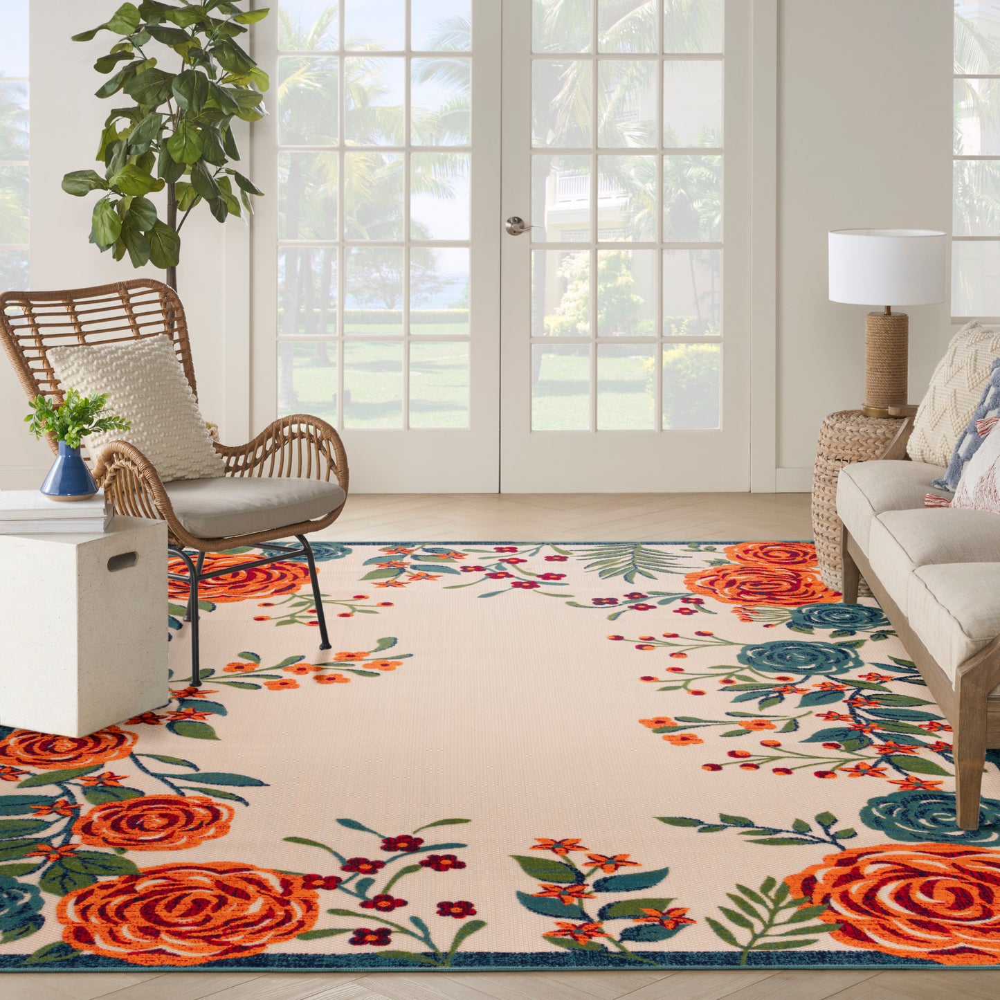 Outdoor space with a large floral area rug featuring orange roses & teal accents on beige, with wicker seating.