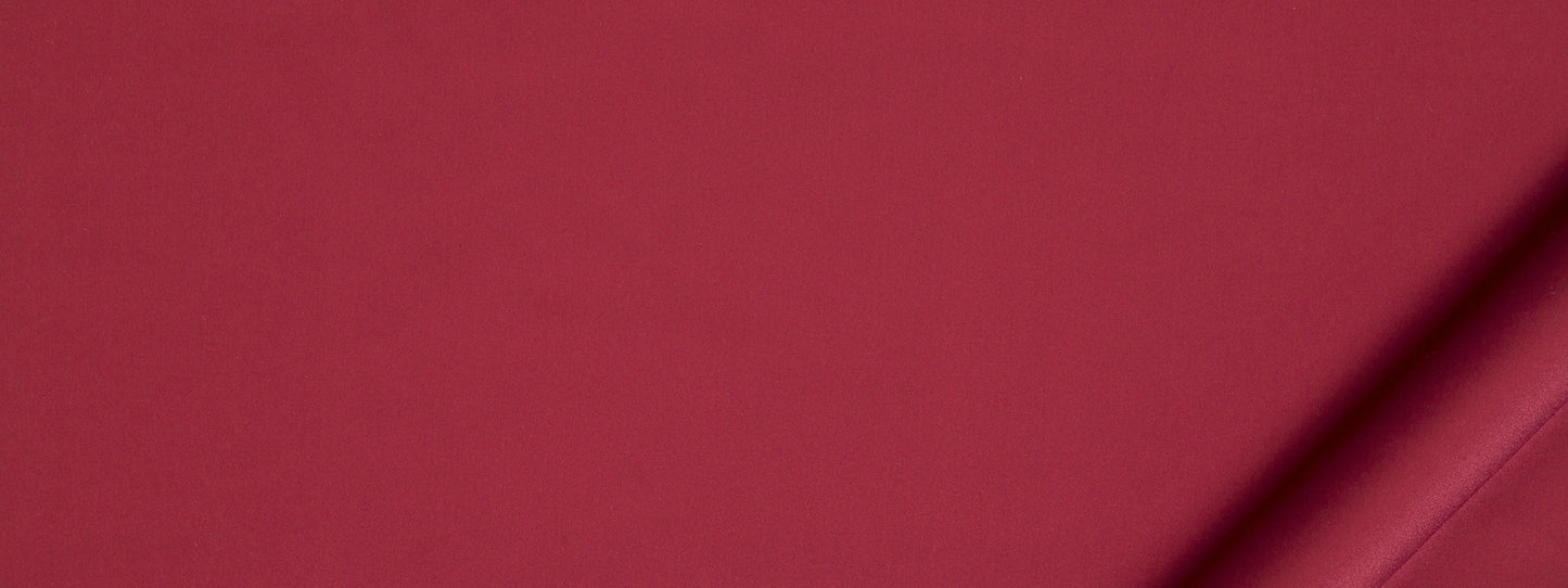 Crimson upholstery fabric with a diagonal fold at bottom-right, smooth matte texture.