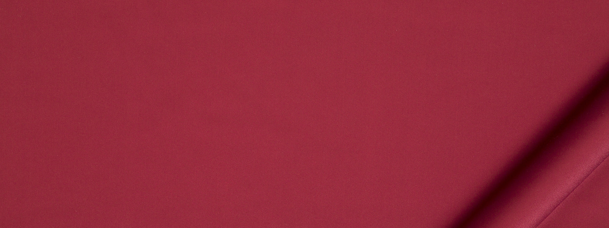 Crimson upholstery fabric with a diagonal fold at bottom-right, smooth matte texture.