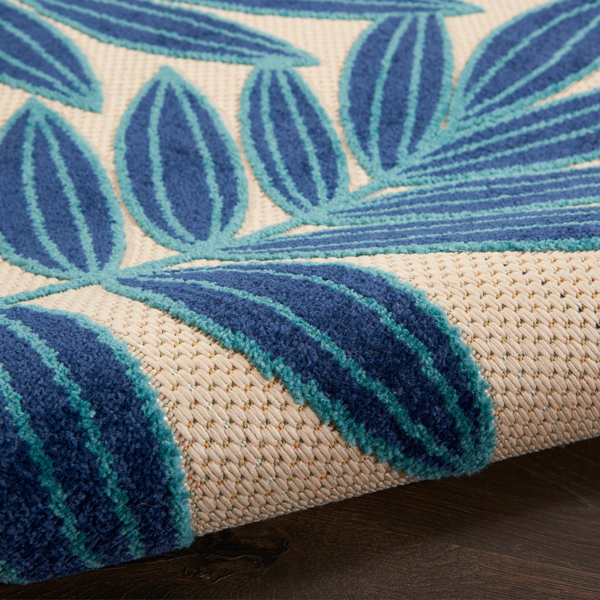 Close-up of beige woven rug with blue leaf pattern and turquoise accents, textured jute weave.