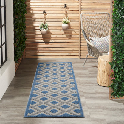 Outdoor runner rug in blue & beige geometric diamonds on a wooden patio with hanging planters & wicker chair.