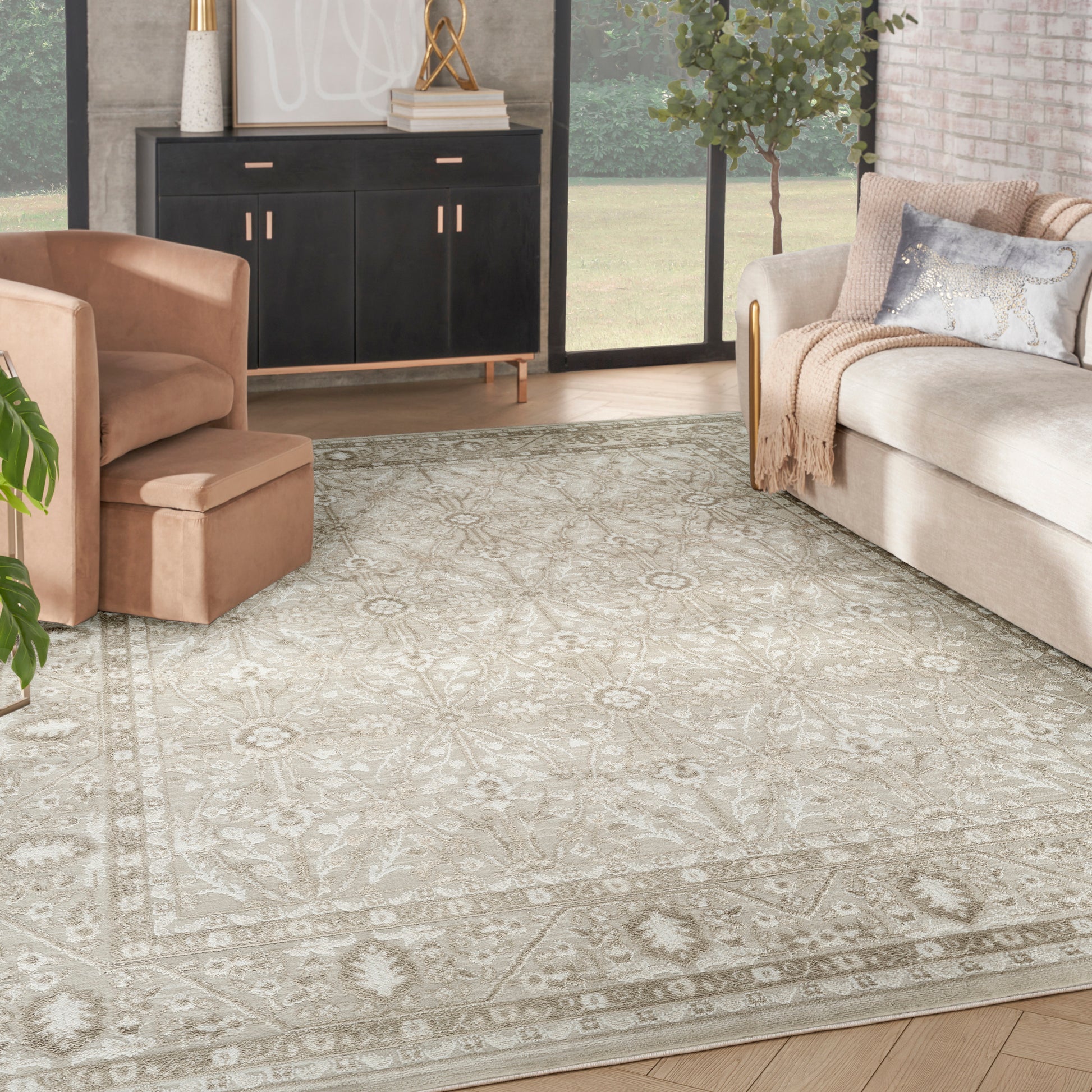 Beige floral-patterned area rug in a modern living room with tan chair, beige sofa, black cabinet, and greenery.
