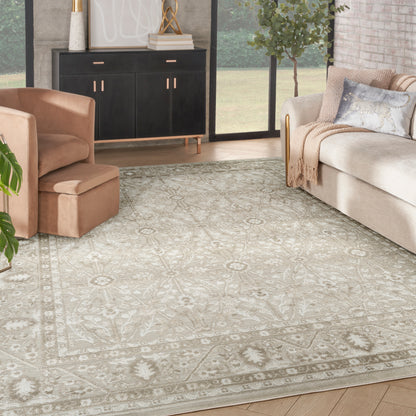 Beige floral-patterned area rug in a modern living room with tan chair, beige sofa, black cabinet, and greenery.