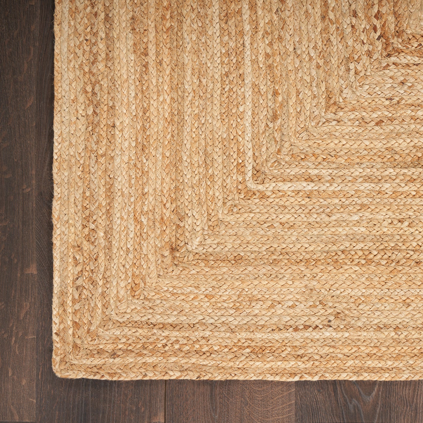 Natural jute rug with braided border in beige tones, layered rectangular weave on dark wood floor.