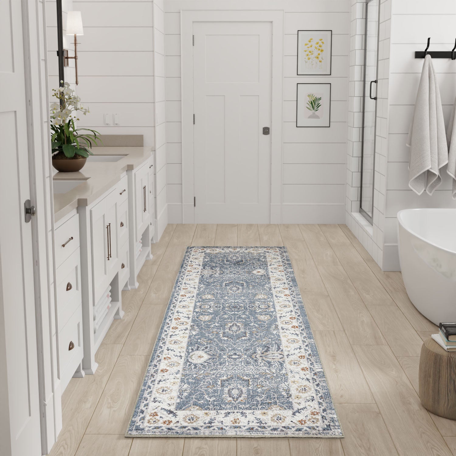 Blue and white Oriental runner rug in a white farmhouse bathroom with vanity, plant, freestanding tub, and botanical art.