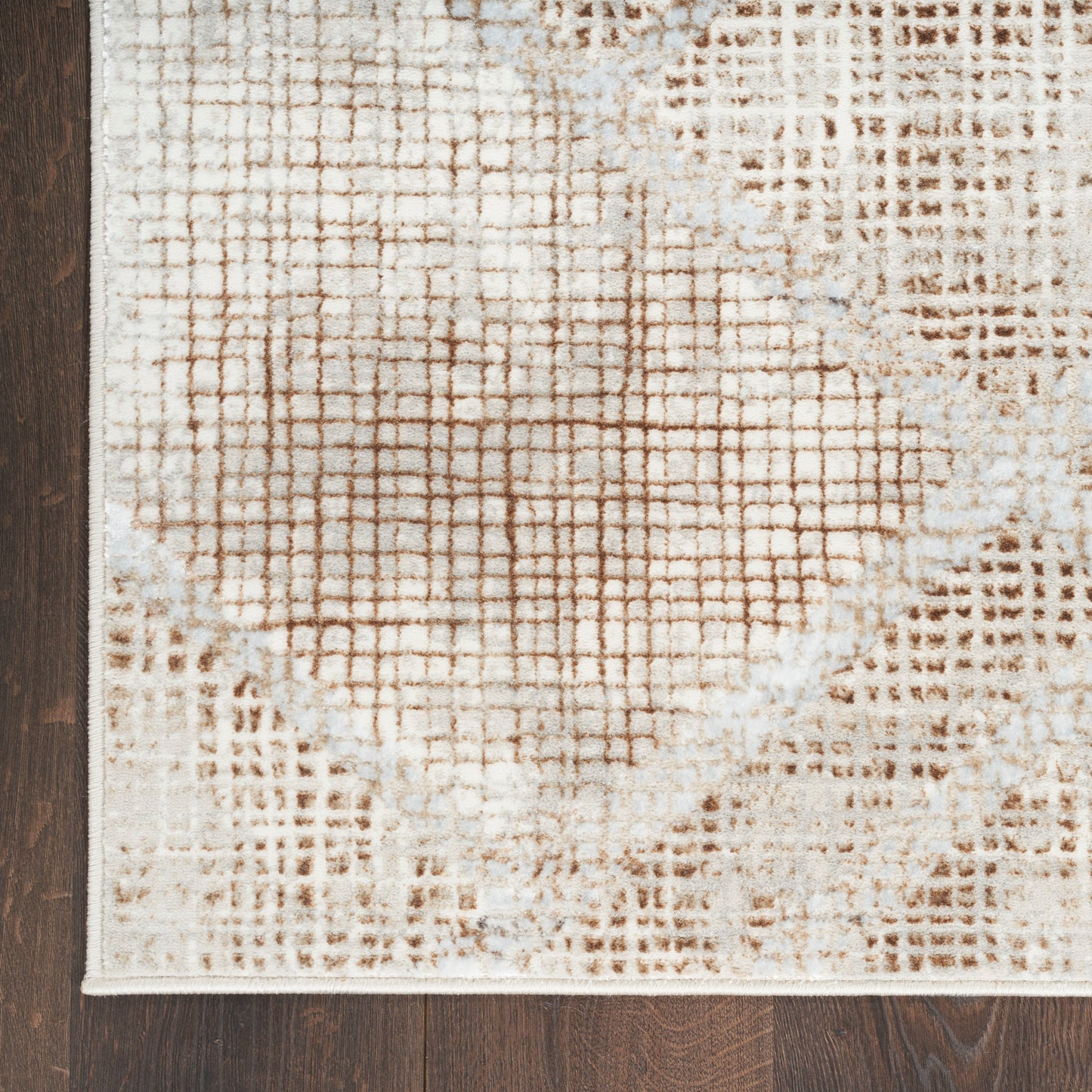 Beige and brown abstract area rug with grid pattern and circular faded rings on dark wood floor.