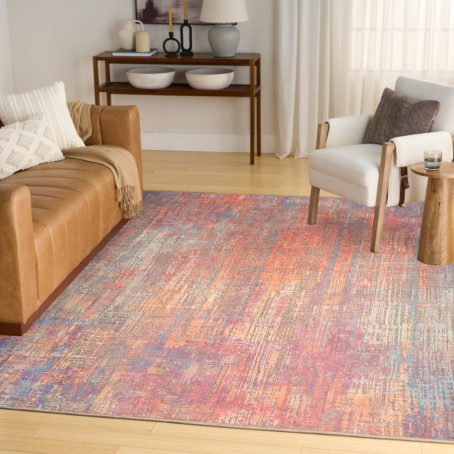 Living room with a tan leather sofa, white armchair, and a multicolor rug in pink, blue & orange; wooden console.