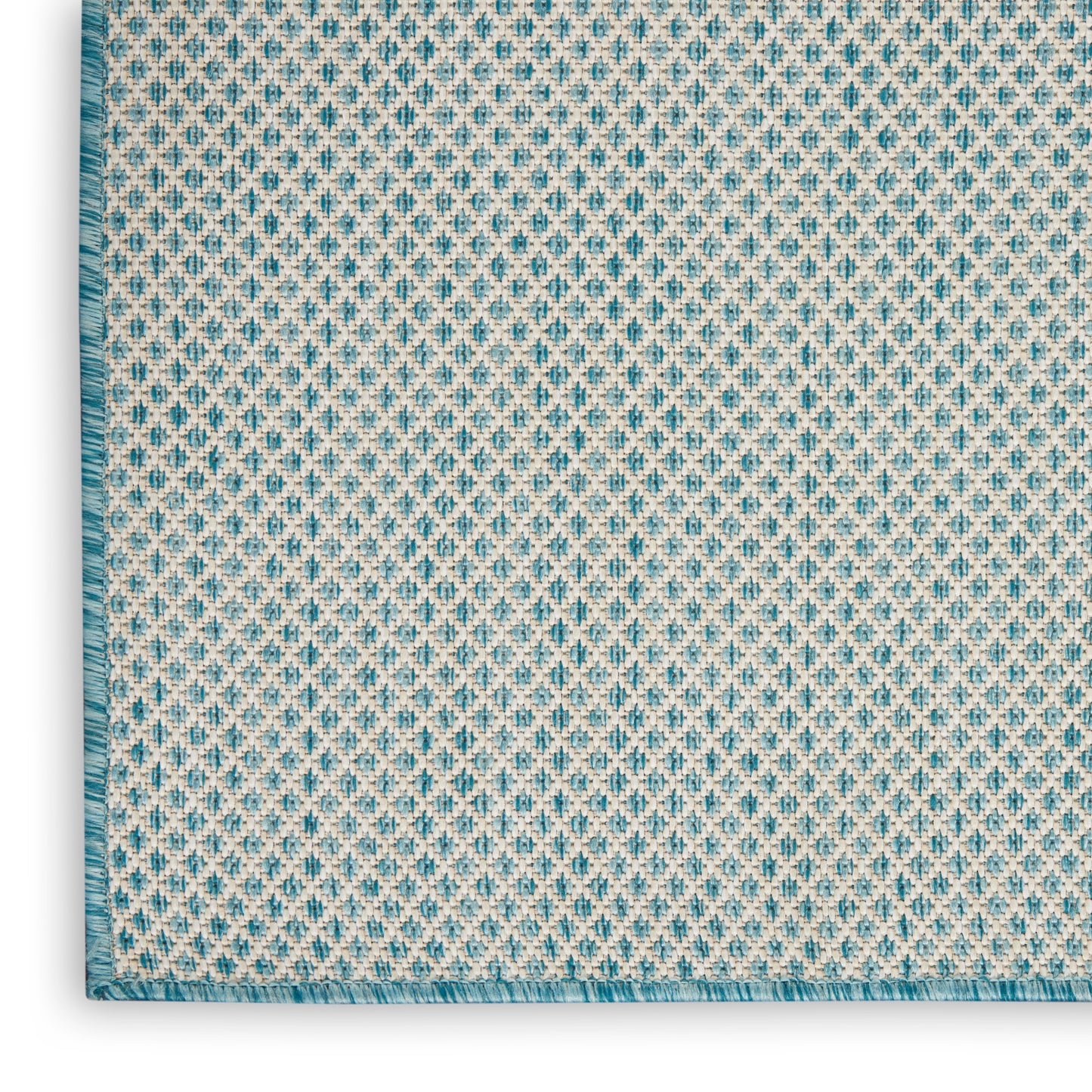 Close-up of a woven textile rug with a blue diamond pattern on ivory, teal fringe along the left edge.