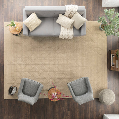 Top-down view of a living room: light gray fabric sofa with beige throws, two gray chairs, tan geometric rug, plants.