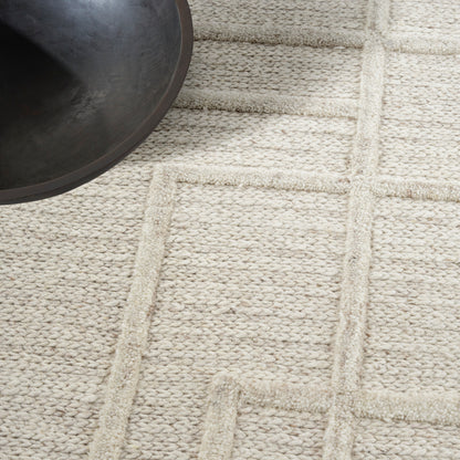 Beige woven rug with a raised rectangular grid pattern; dark round bowl edge peeks into the top-left corner.